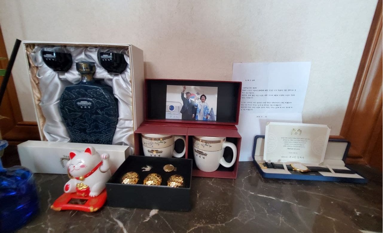 뉴스버스가 입수한 수산업자 김태우 자택 벽면 사진. 사진에는 청와대 로고가 새겨진 술병과 술잔, 머그컵 세트, 시계, 문재인 대통령과 김정숙 여사의 사진, 문 대통령 부부 명의 새해 인사 카드가 찍혀있다. (사진=뉴스버스)