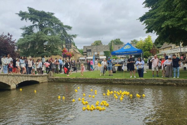 중세 마을 코츠월드에서 장난감 오리 경주를 즐기는 관광객.