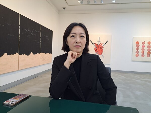 고영미 작가. 왼편 '젖과 꿀이 흐르는 땅, 162×360cm, 2024'은  별이 반짝이는 검은 하늘에 회색 전투기들이 정면을 응시하며 날아오르는 모습이다. (사진= 심정택)